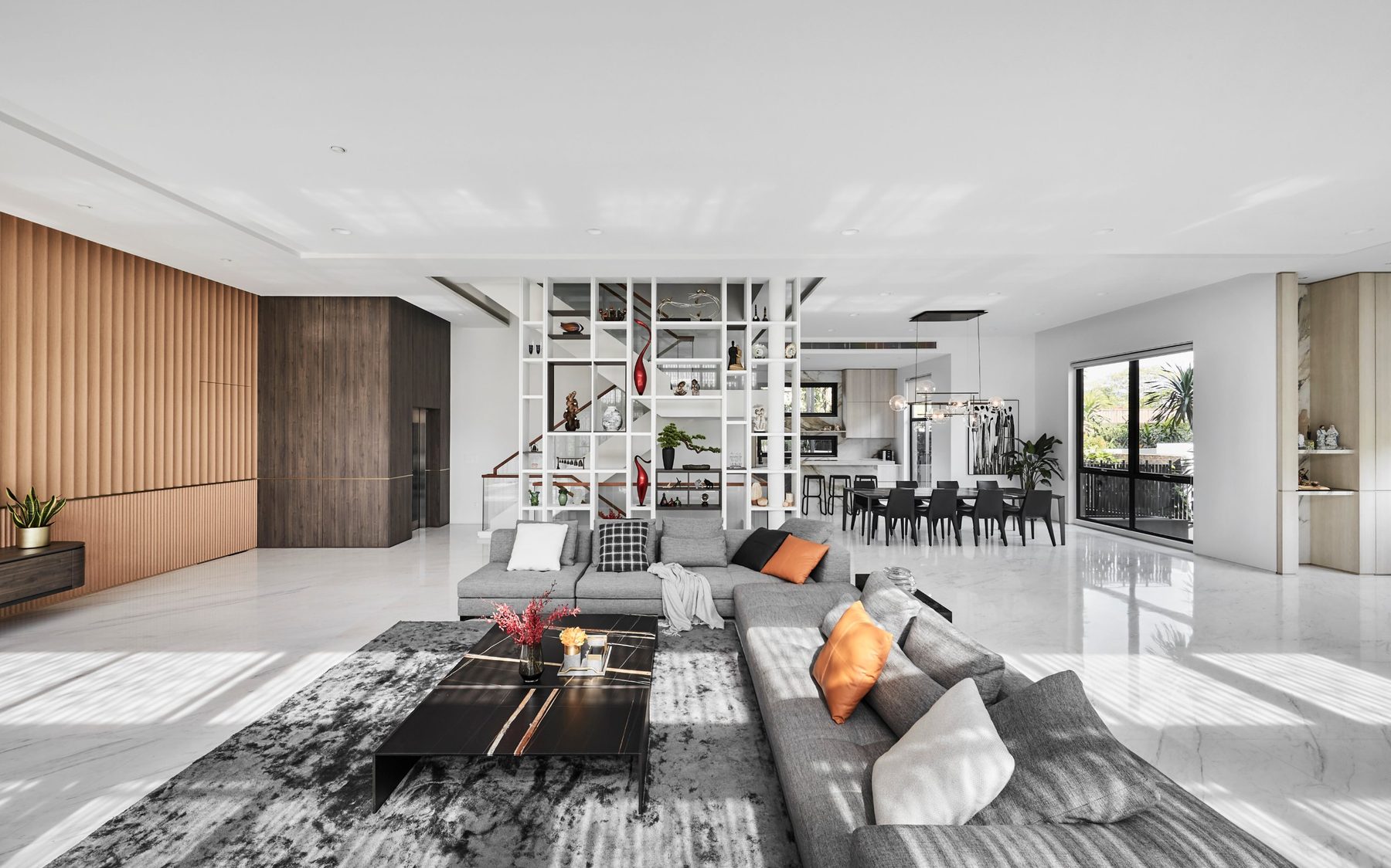 Open-plan living room with a white shelving partition, grey sectional sofa and wood-panelled feature wall at the Namly Hill residence