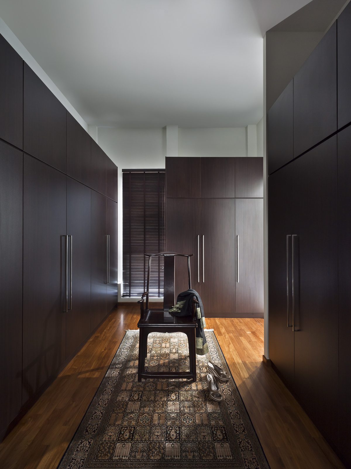 Walk-in wardrobe lined with dark timber cabinetry and a carved wooden chair on a patterned rug, Green Leaf (2011)