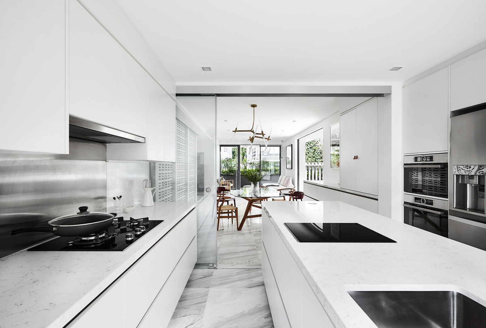 A white kitchen with marble counter tops and stainless steel appliances.