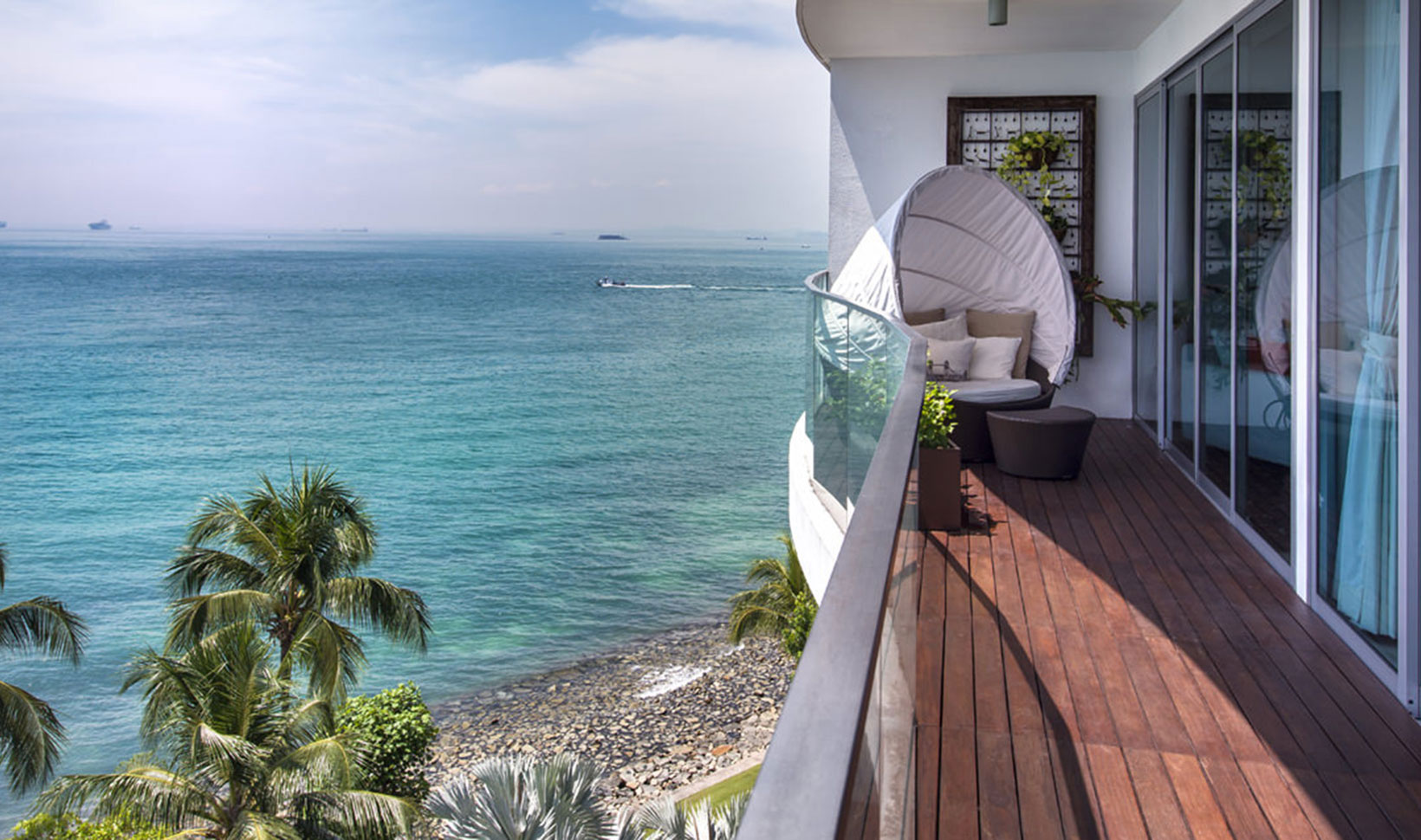 A balcony overlooking the ocean and palm trees.