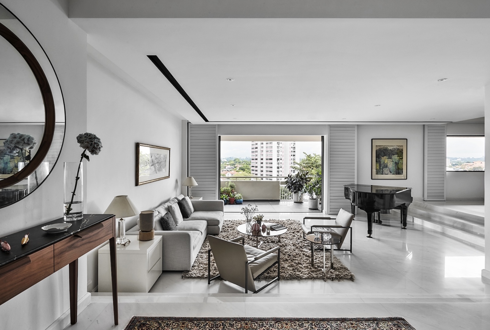 A modern living room with a sofa, armchairs, a coffee table, a console table with a round mirror, art on the walls, a piano, and large windows offering a city view.